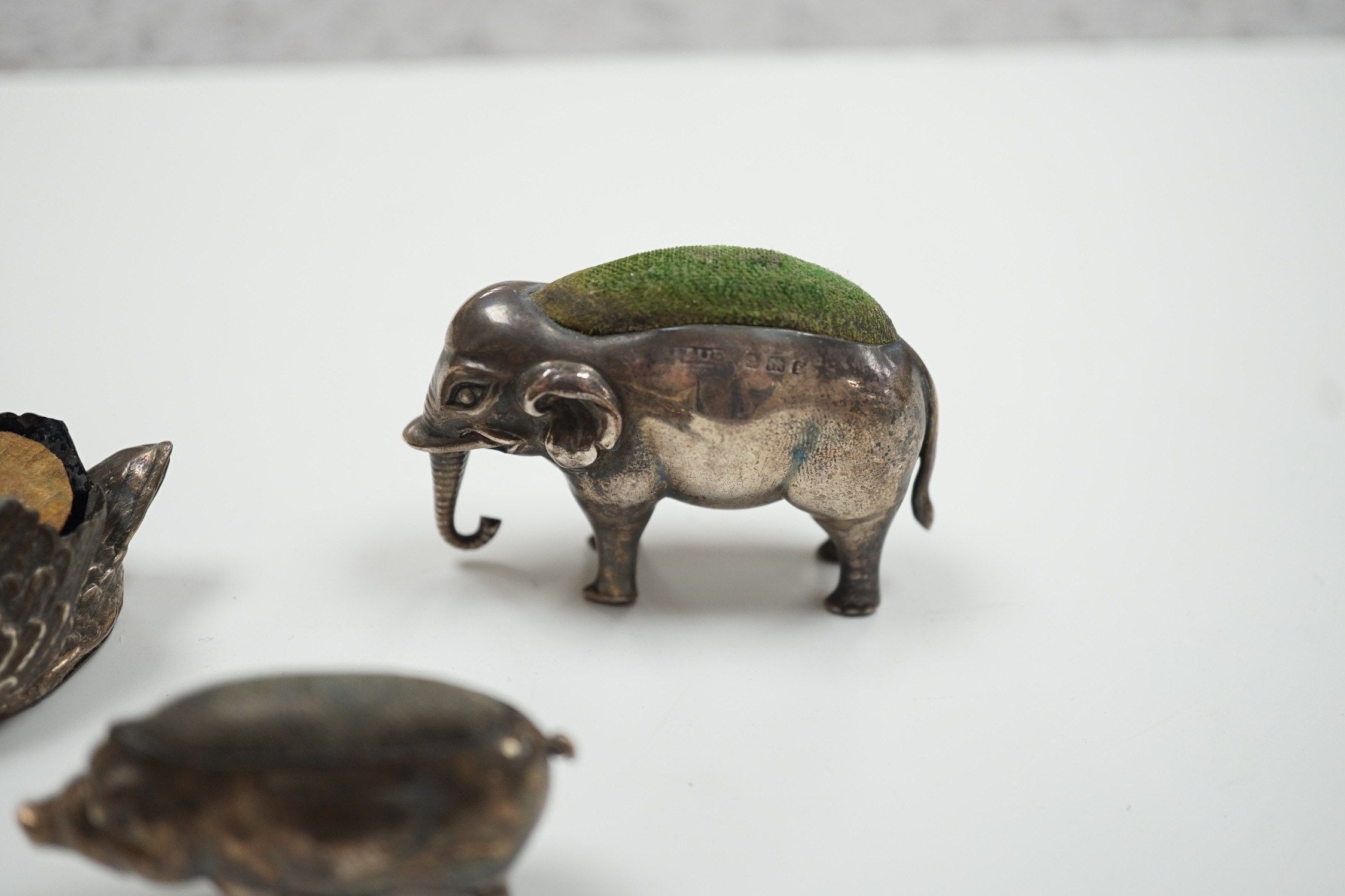 An Edwardian silver elephant pin cushion, Adie & Lovekin, Birmingham, 1905, length 62mm, a similar pig and late Victorian swan pin cushions.